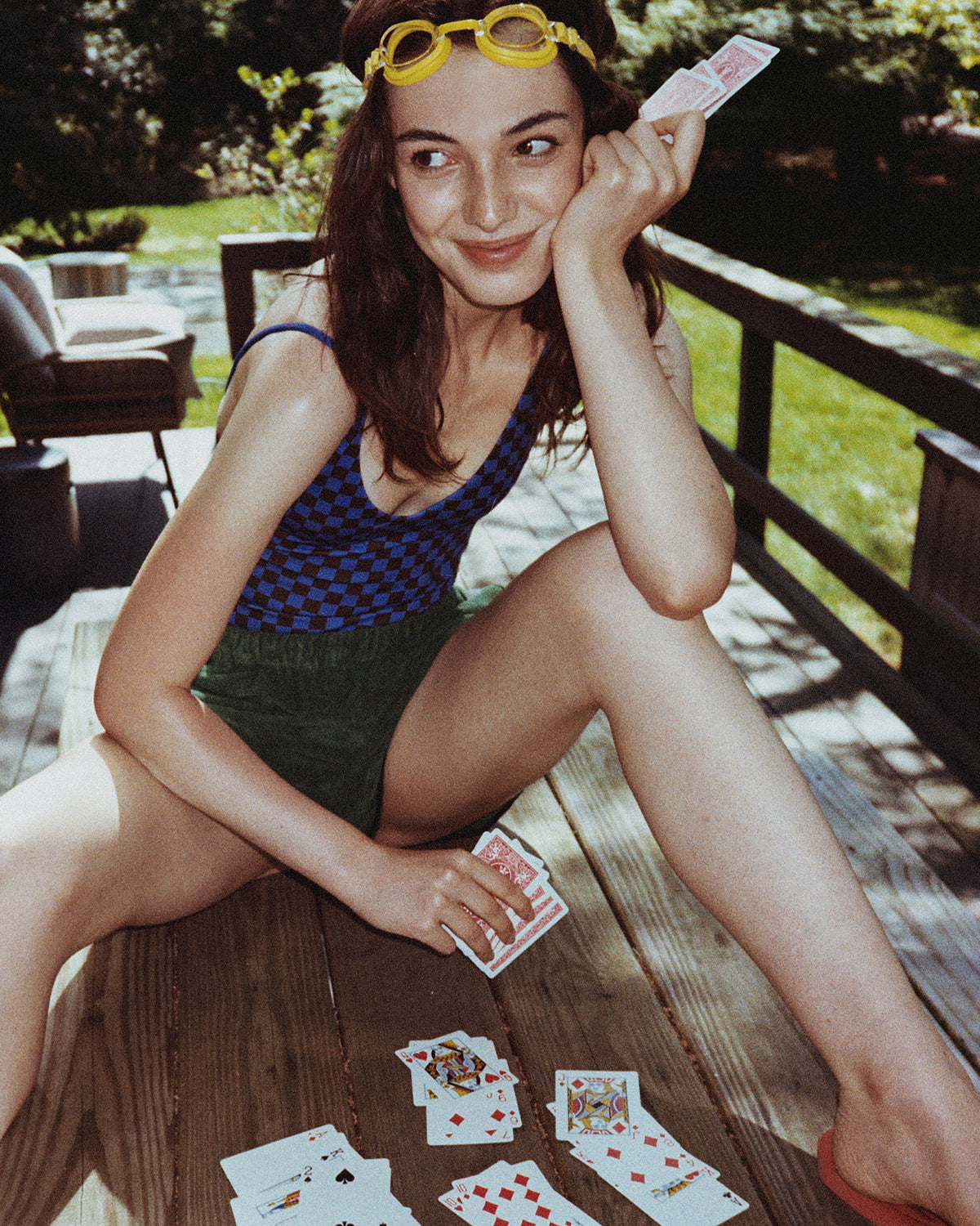 Model sitting on a deck wearing the Sunday Suit in Check It with La Plage Shorts in Basil. 