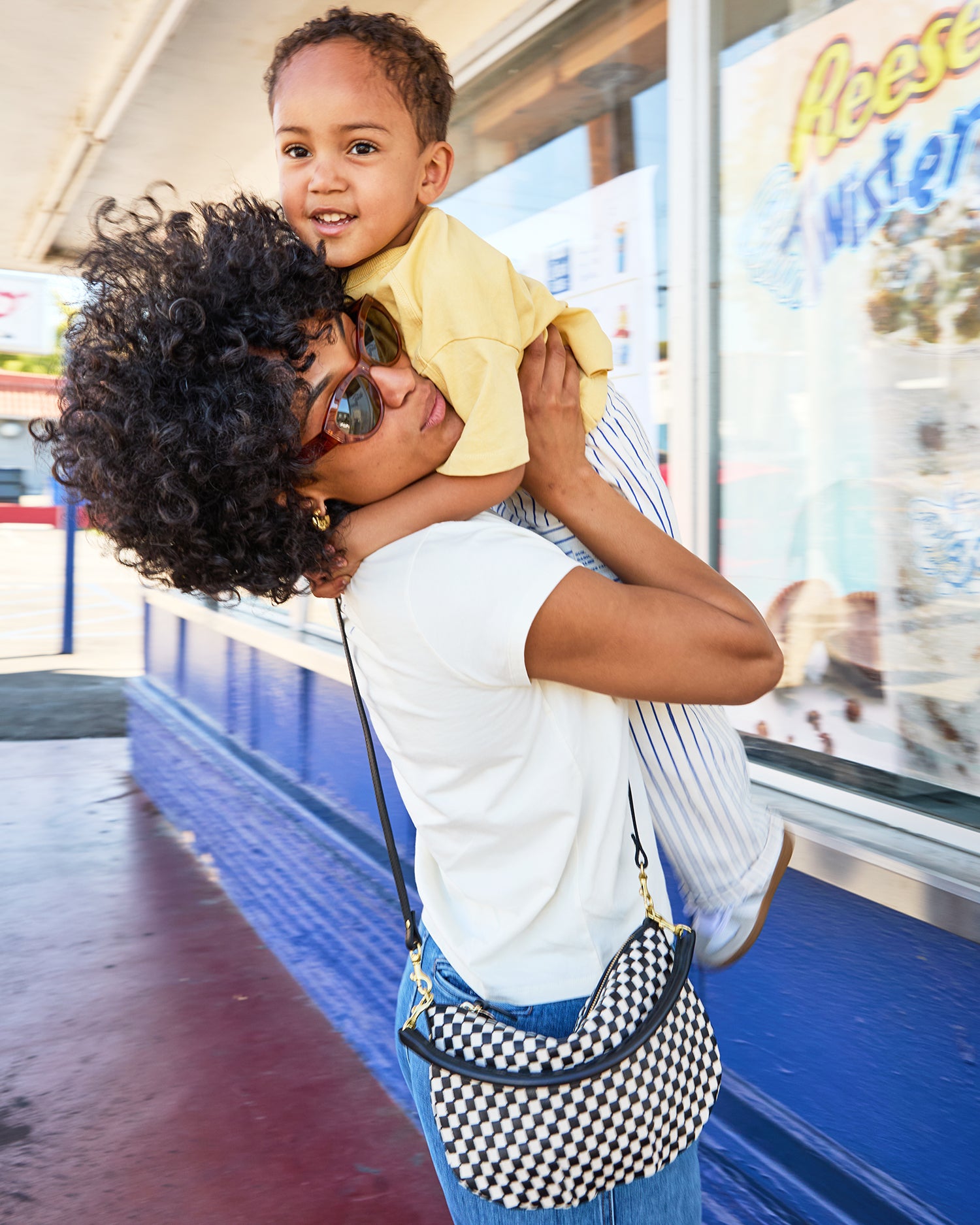 Mother wearing a black and cream checker petit moyen while carrying her child. 
