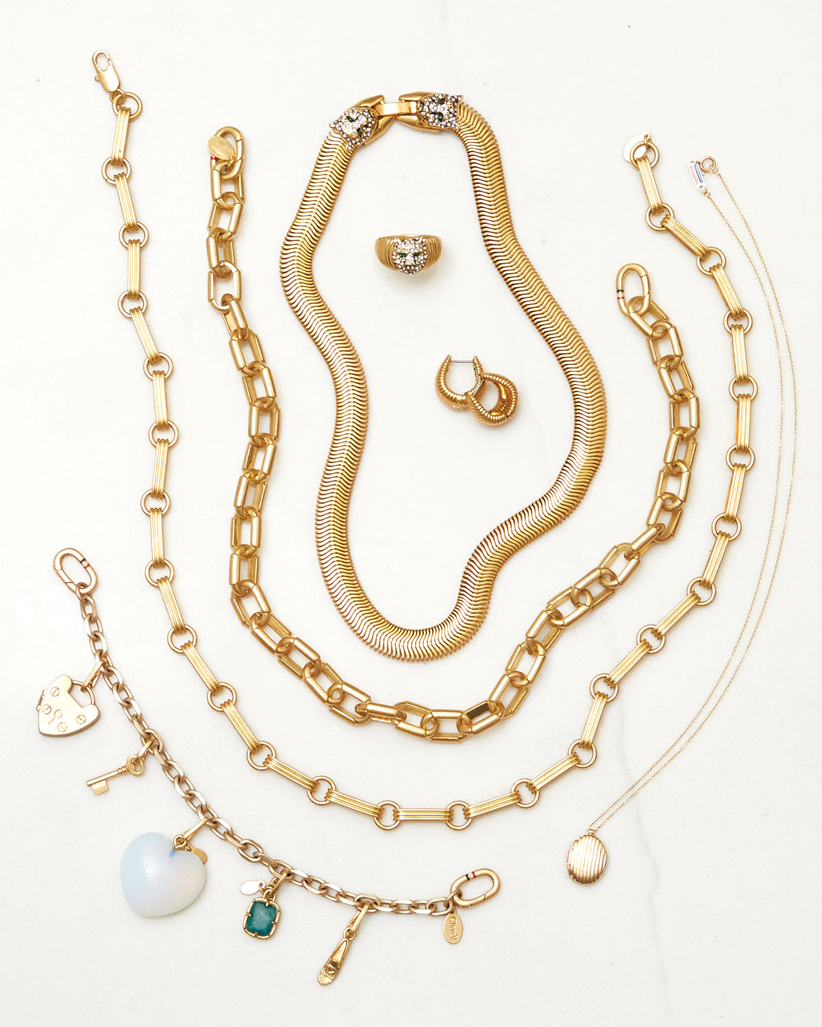 Assortment of Clare V. jewelry. Items featured: Whiskers Signet Ring, Ridge Huggie Earrings, Snake Chain Collar, Le Link Necklace, Charm Bracelet with assorted charms, Ridge Locket Necklace. 