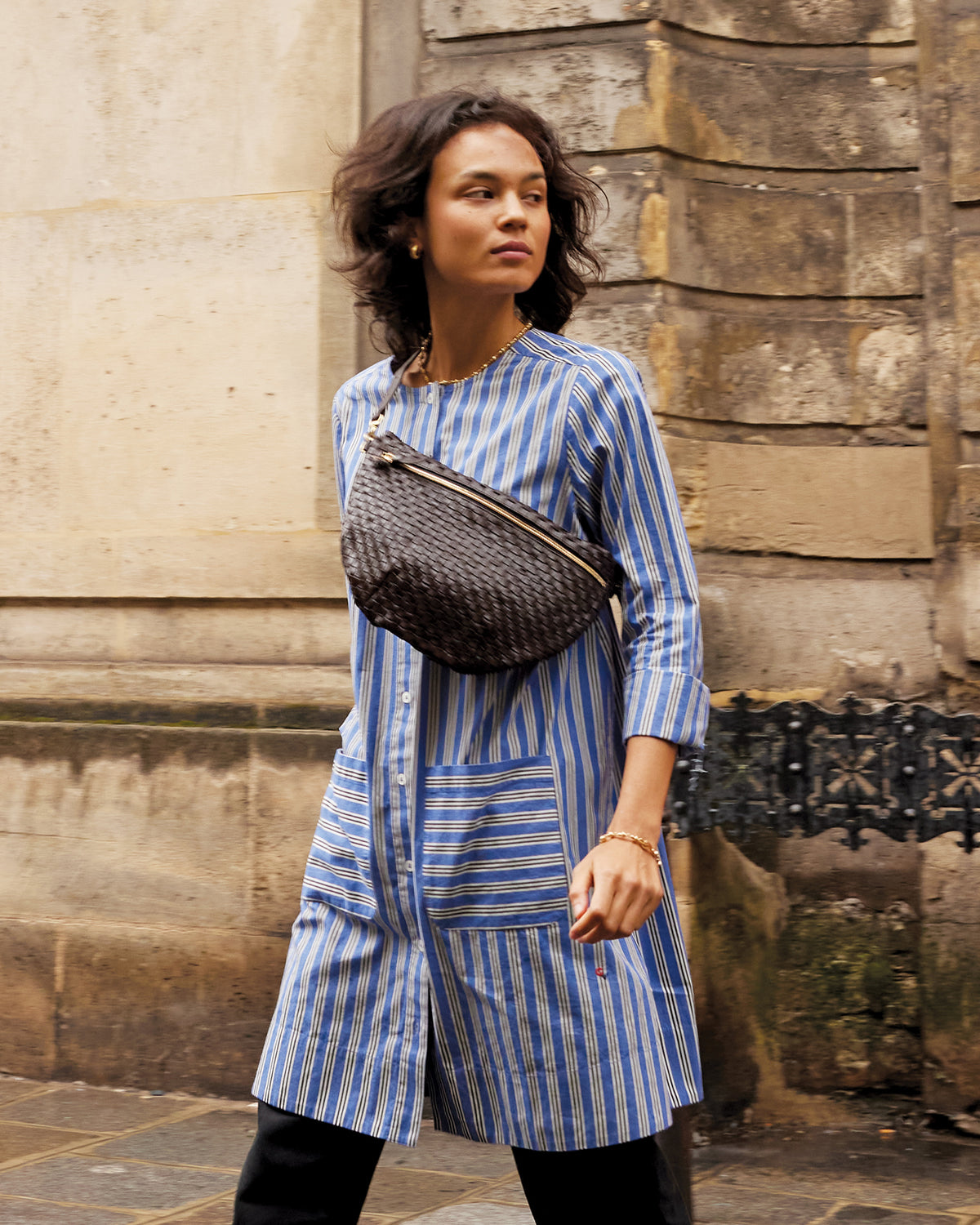 Model wearing the Mariette Dress in Maroq Stripe and carrying the Kalamata Woven Checker Grande Fanny across her chest.