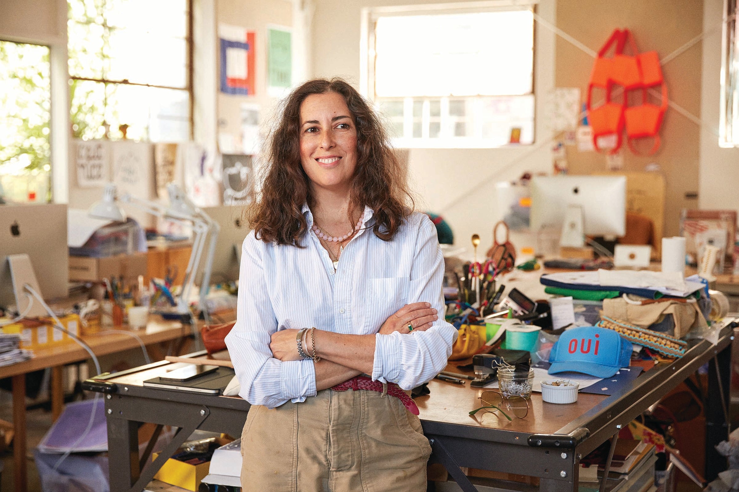 Clare Vivier standing in front of a desk smiling with her arms crossed. She's in her studio located in Los Angeles, CA. 