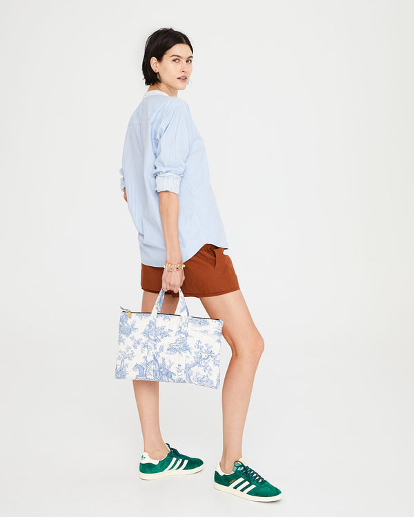 Athena posing with the St. Calais Blue Quilted Linen Toile Laptop Case. Athena is wearing a blue shirt and brown shorts. 