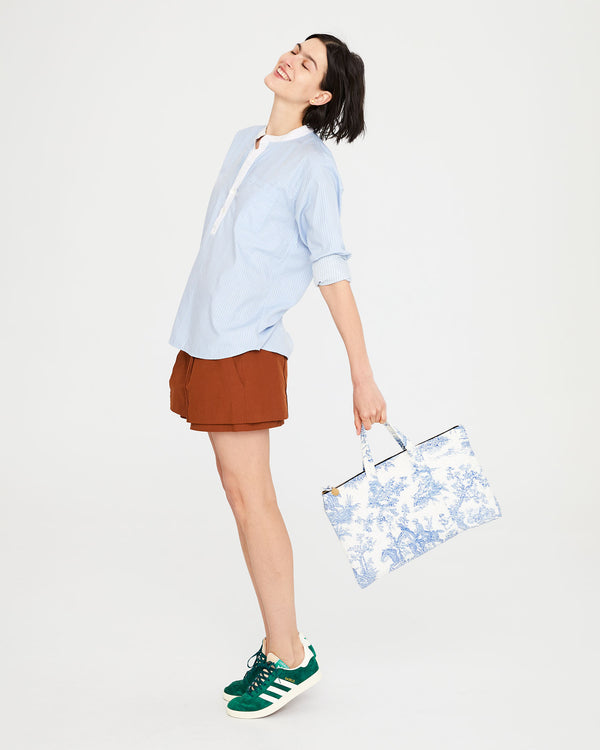 Athena standing on her tip toes while swinging the St. Calais Blue Quilted Linen Toile Laptop Case.
