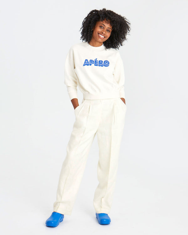 mecca with her hands in the pockets of her white slacks. she's also wearing the Cream Apéro Le drop with blue clogs