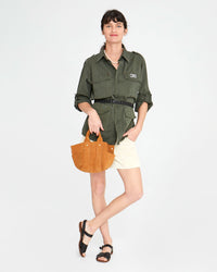 danica holding the Le Petit Box Tote in Camel Suede in front of her crossed legs