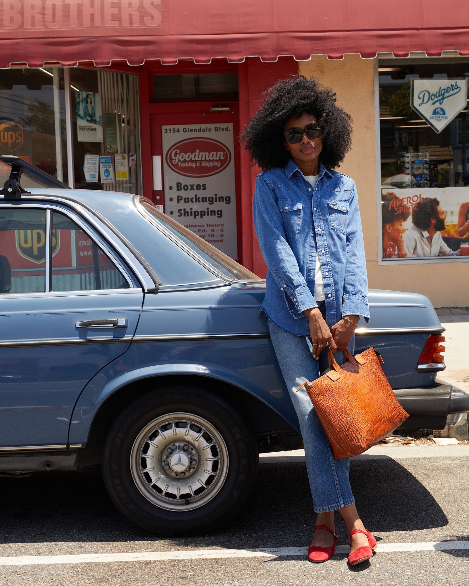 Mecca leaning against a blue car with the Cuoio Croco Le Zip Sac