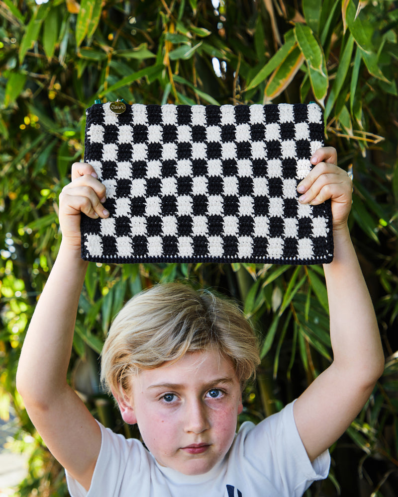 Child holding the Black and Cream Crochet Checker Flat Clutch with Tabs.