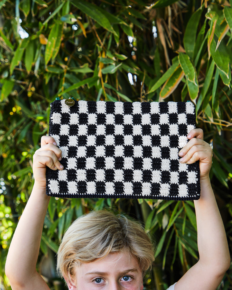 Child holding the Black and Cream Crochet Checker Flat Clutch with Tabs.