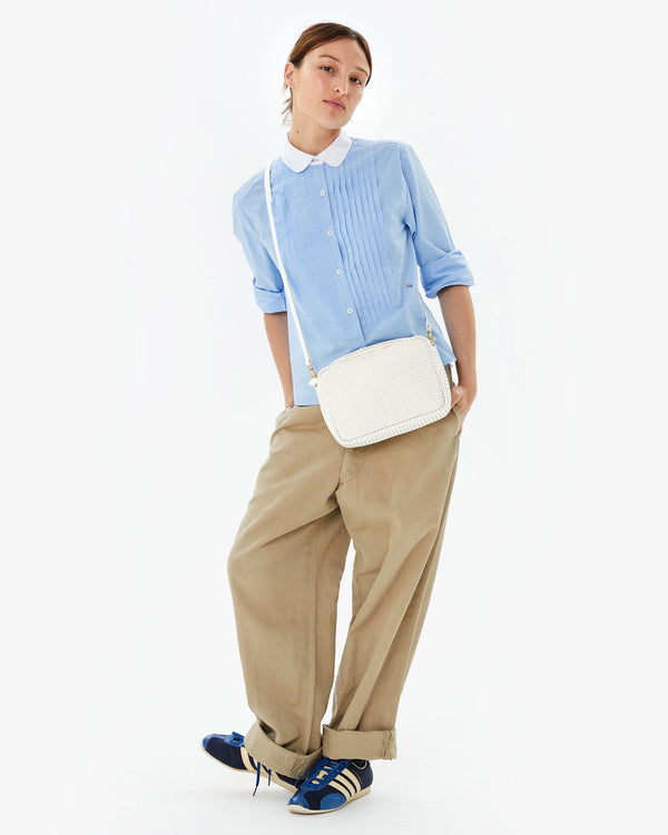 Zoe in tan pants and a blue top with the Brie diagonal woven Marisol worn crossbody. her hands are in the pockets of her pants