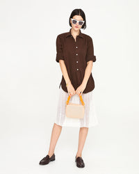 Athena wearing a brown shirt and a white skirt. she's carrying the Ballet Perf Midi Sac by the neon orange resin shortie strap