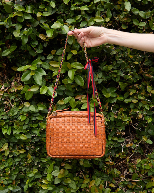 Katie holds the Natural Woven Midi Sac in front of a bush