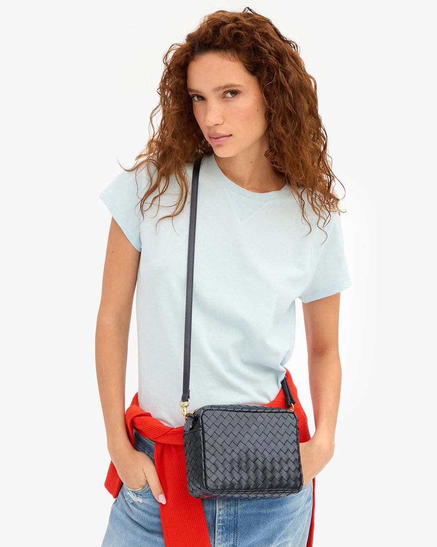 Model wearing a light blue t-shirt with jeans and carrying the Twilight Diagonal Woven Midi Sac as a crossbody bag.
