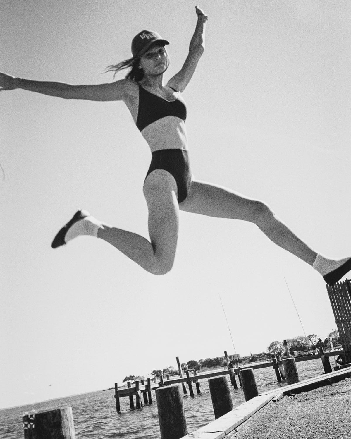 Model wearing  a CV x Left On Friday 2-piece swimsuit with CV x Left On Friday Trucker Hat. 