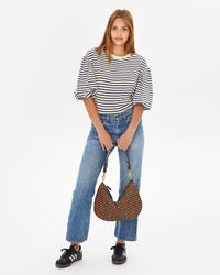 aurelia holding the Black & Natural Woven Checker Moyen Messenger in front of her jeans by its shoulder strap