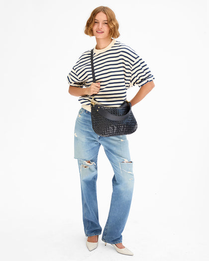 Model wearing the cream and navy Short Sleeve Oversized Sweatshirt, distressed light blue jeans, and white shoes and carrying the Twilight Diagonal Woven Moyen Messenger as a crossbody bag using the crossbody strap the bag comes with. 