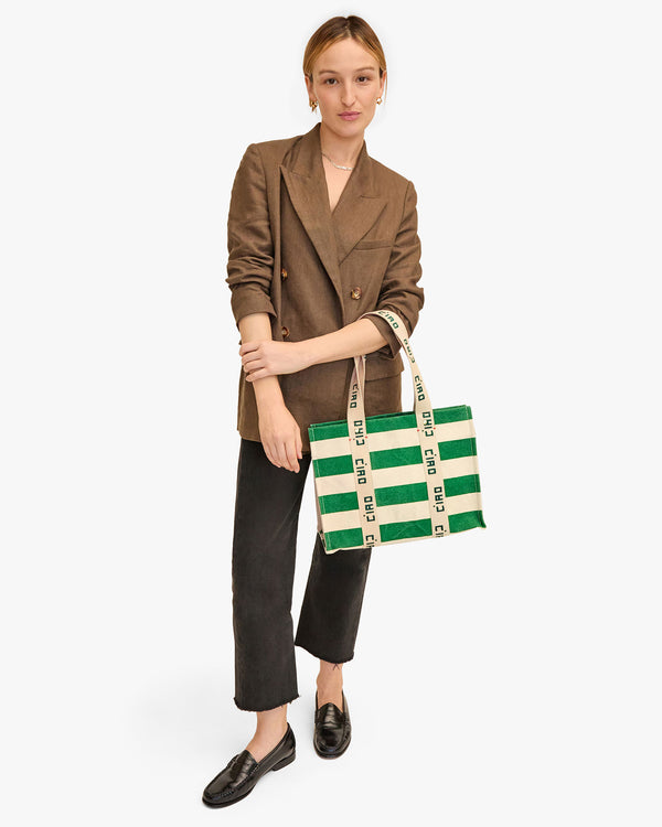 Zoe holds the Noemie Canvas Tote in Palm Green and Natural Stripe in the crook of her elbow