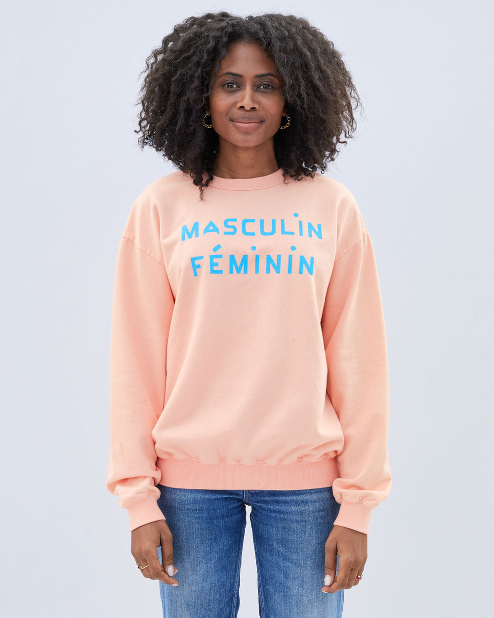 Mecca wearing the  Coral with Light Blue Masculin Feminin Oversized Sweatshirt untucked with blue denim jeans