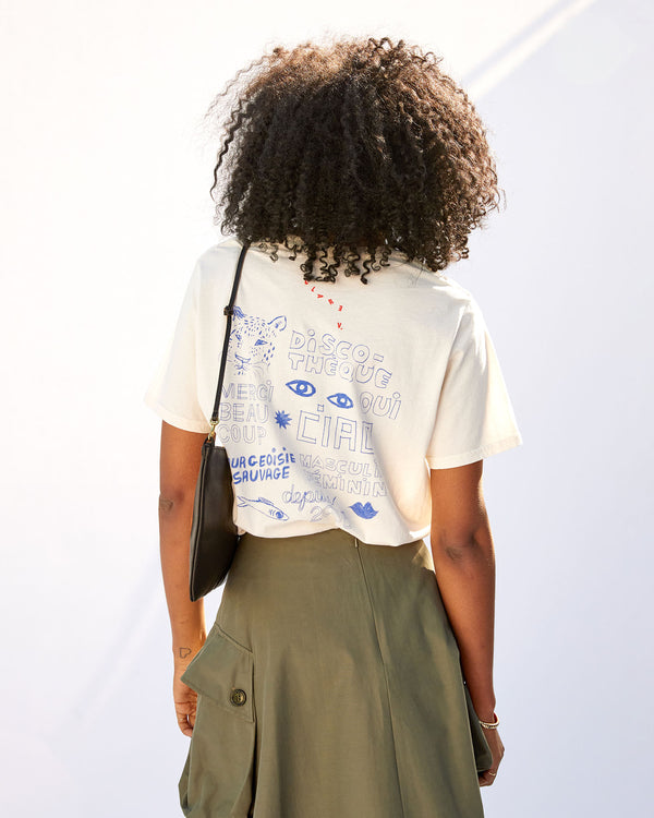 back view of mecca wearing the Cream Bourgouise Sauvage Original Tee tucked in to an army colored skirt