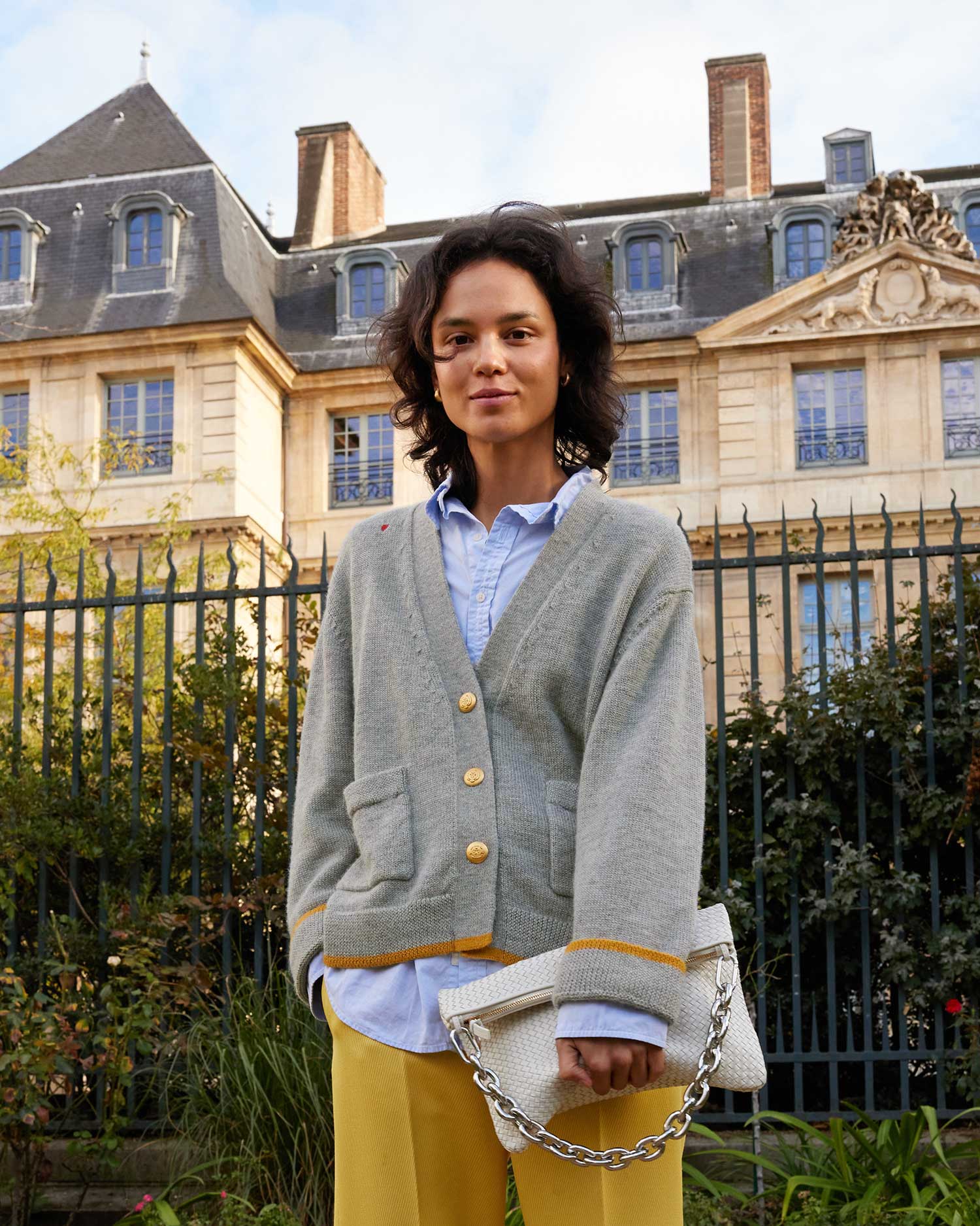 Gabrielle wearing the Oscar Sweater in Cloud over a blue button up shirt and yellow pants