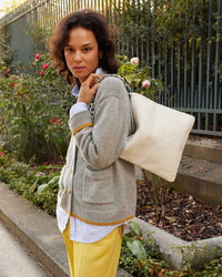 Gabrielle with the brie woven foldover clutch with tabs on her shoulder in the Oscar Sweater in Cloud and yellow pants