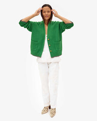 Maly tucking her hair behind her ears in white overalls and the Oscar Sweater in Granny Smith