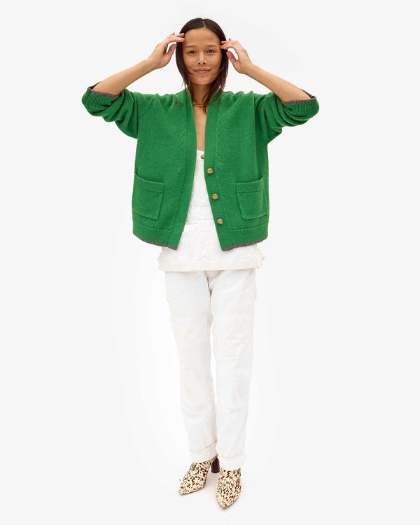 Maly tucking her hair behind her ears in white overalls and the Oscar Sweater in Granny Smith