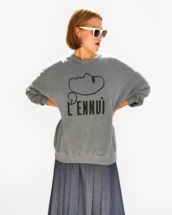 Sonnie wearing the Grey L'Ennui Oversized Sweatshirt with a grey pleated skirt with the cream heather sunglasses. her hands are on her hips