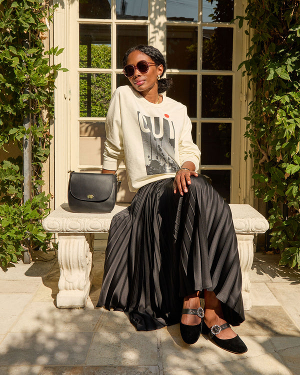 Mecca wearing the cream oui oversized sweatshirt with a black pleated skirt 