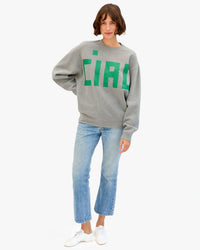 Kathie wears the Oversized Sweatshirt in Grey Melange w Grande Block Ciao and stands with one hand on her hip