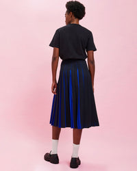 back view of the model wearing the Navy & Black Stripes w/ French Blue Pleats Pleated Skirt with a black tee shirt tucked in