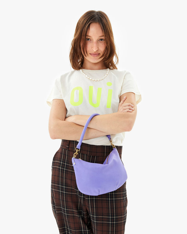 Zoe wears the Cream Oui Classic Tee tucked in to brown plaid pants and carries the violet petit moyen messenger hanging from her arms crossed over her chest