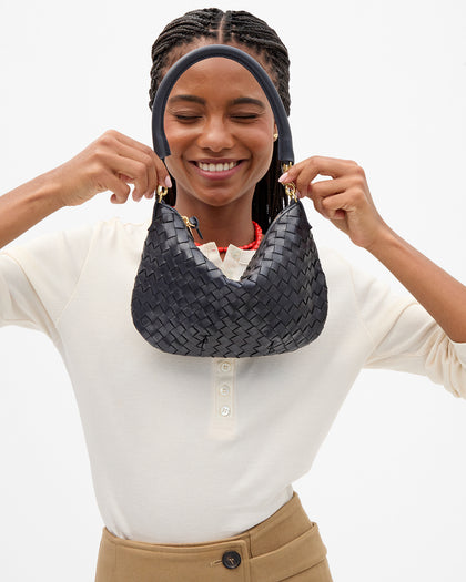 A woman wearing a cream henley shirt and tan pants holding up the Twilight Diagonal Woven Petit Moyen.