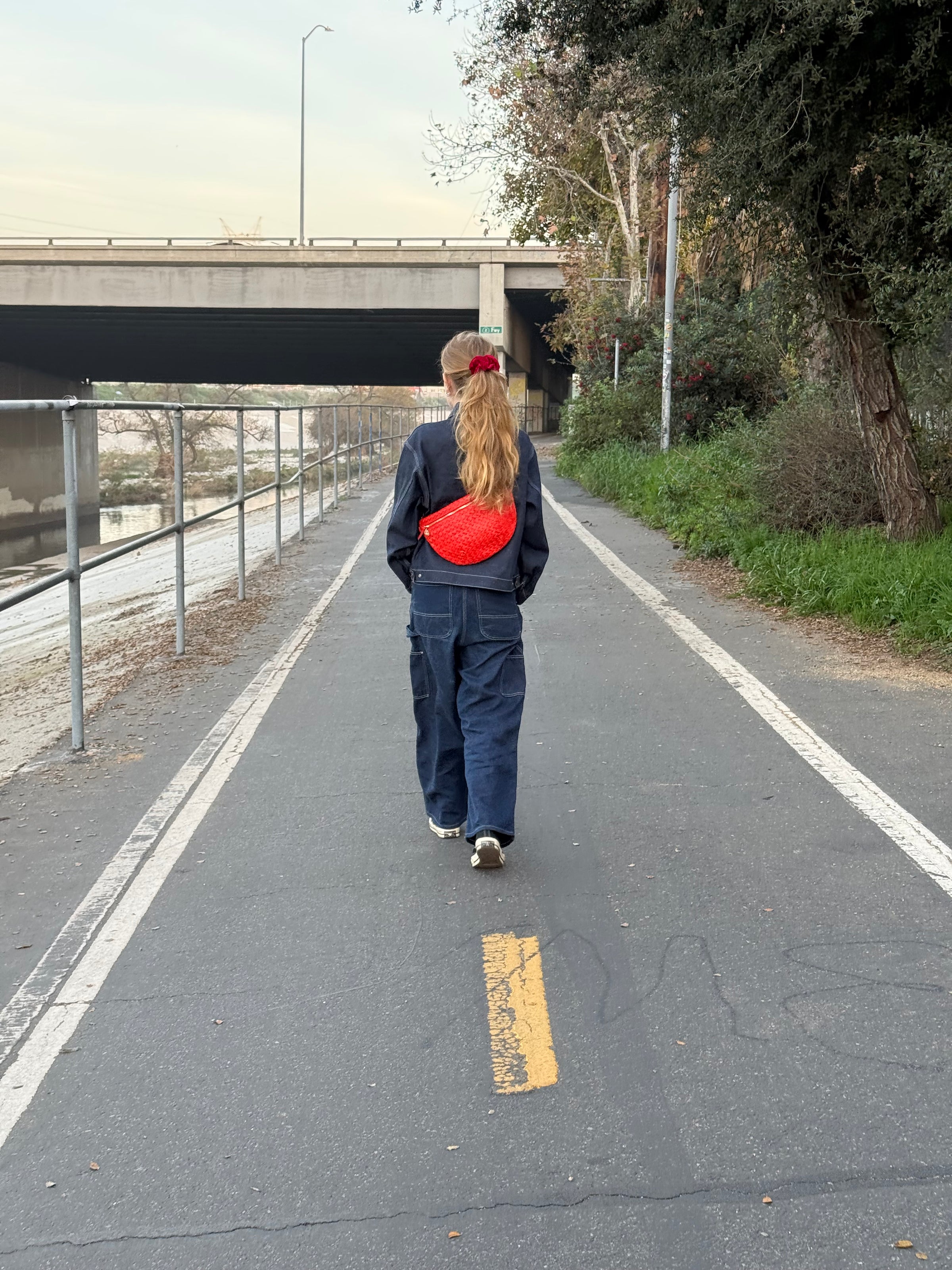 Woman carrying the Bright Poppy Diagonal Woven Grande Fanny across her back.