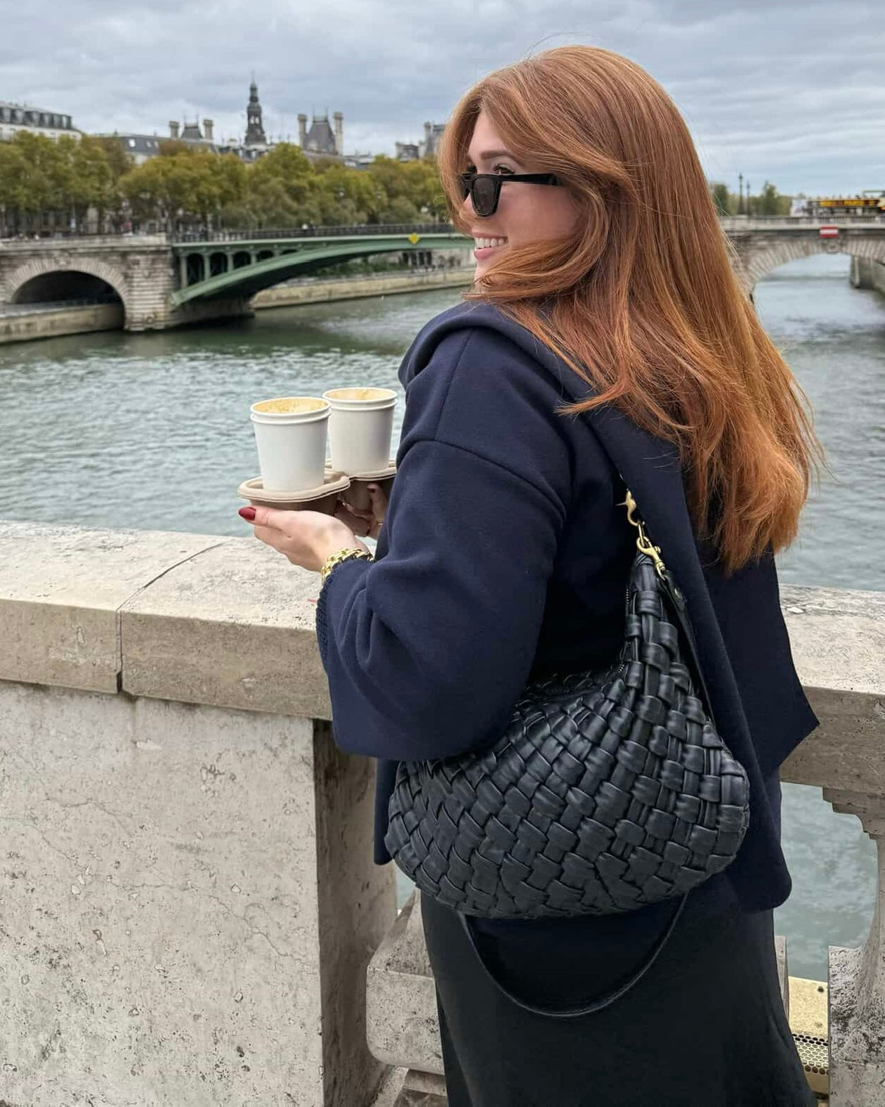 Woman carrying cups of coffee and carrying the Black Puffy Woven Moyen Messenger over her shoulder. 
