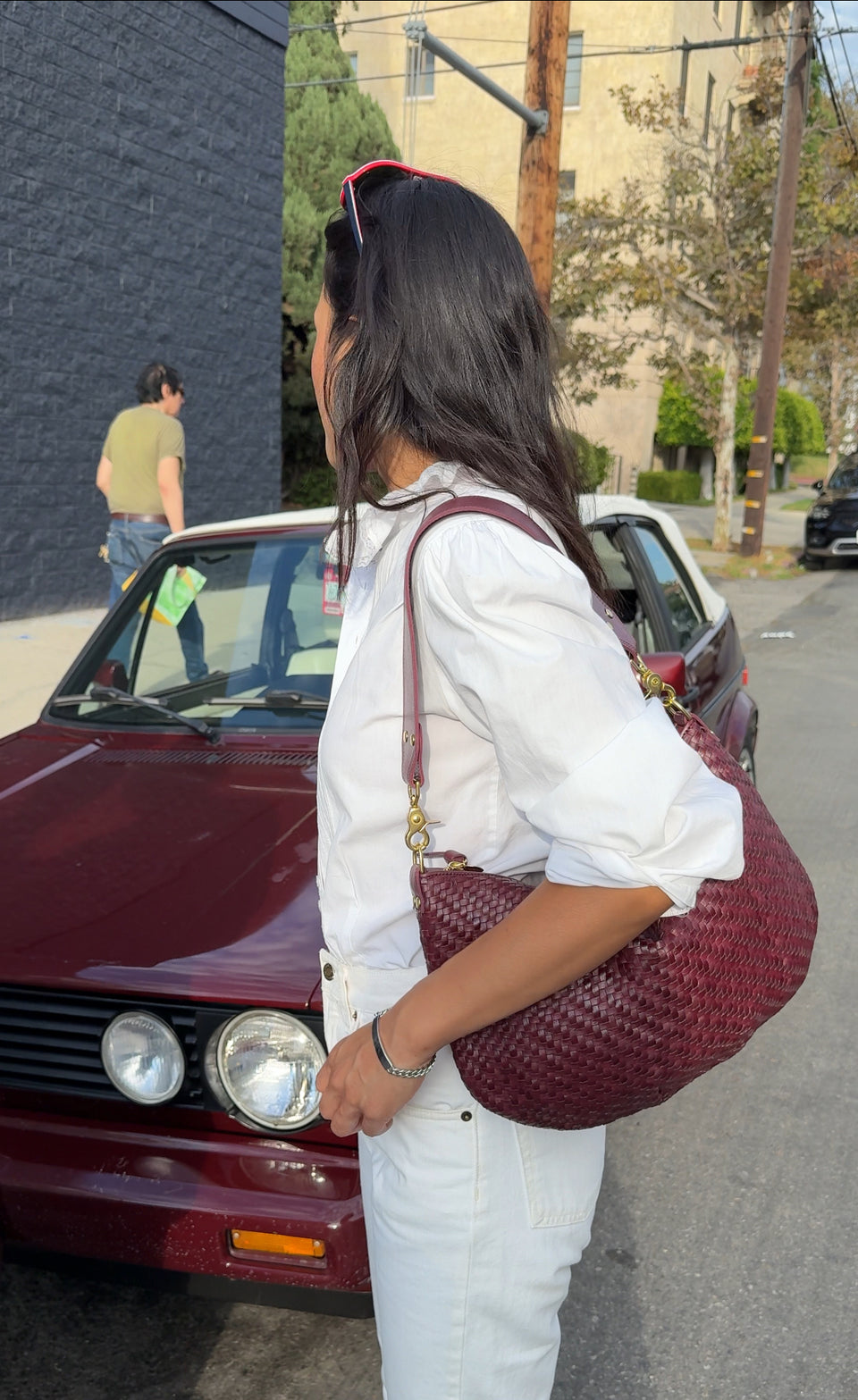 Woman carrying the Cassis Woven Moyen Messenger standing near a car that matches the color of her bag.