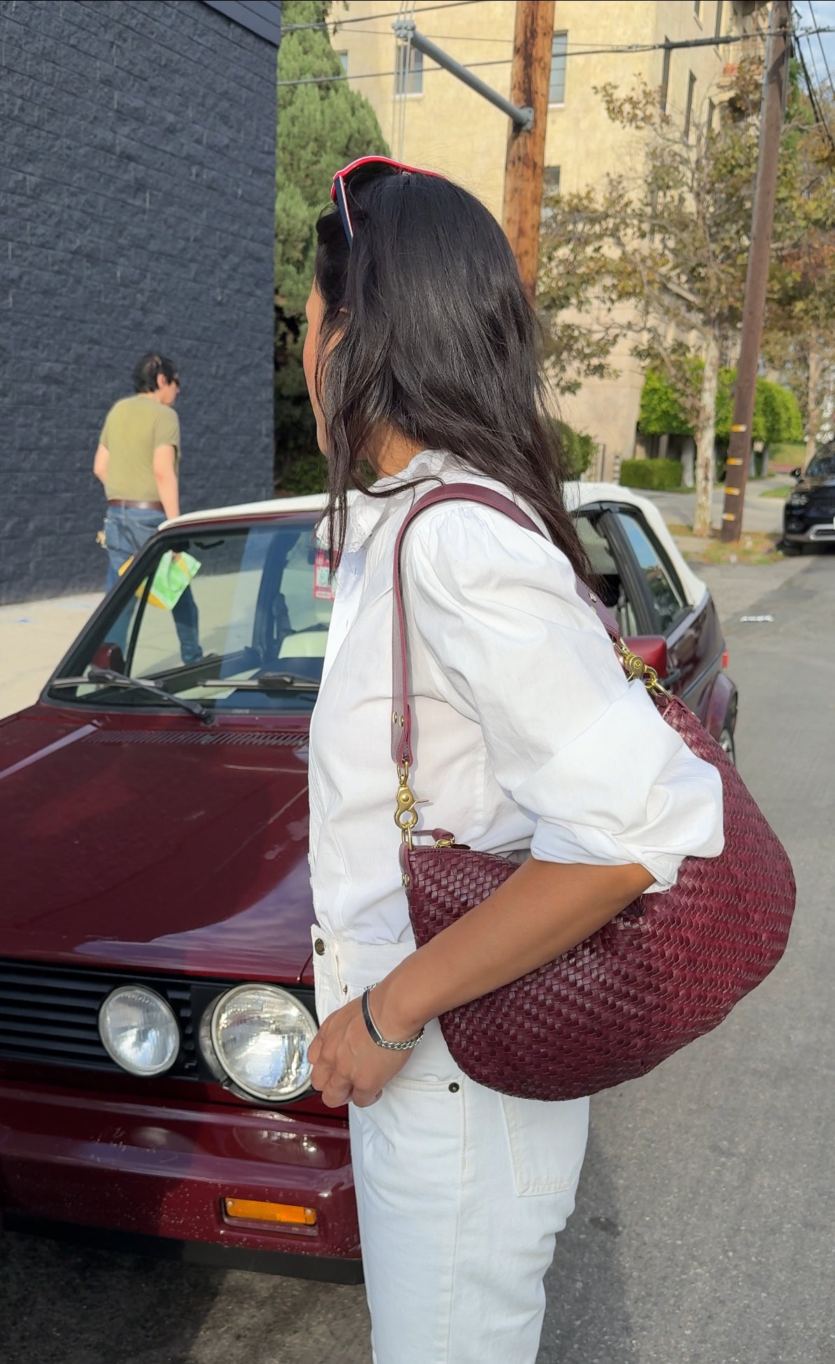 Woman carrying the Cassis Woven Moyen Messenger standing near a car that matches the color of her bag.