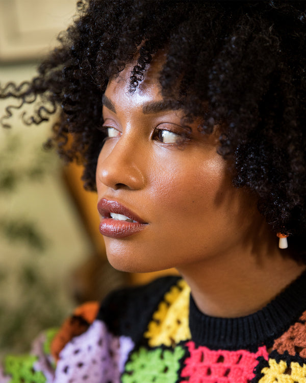 Model wearing a colorful sweater with the Rel Beauty Lip Balm in For Sure