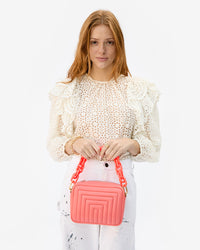 haley holding the Bright Coral Channel Quilted Midi Sac by the bright coral resin shortie strap in front of her stomach
