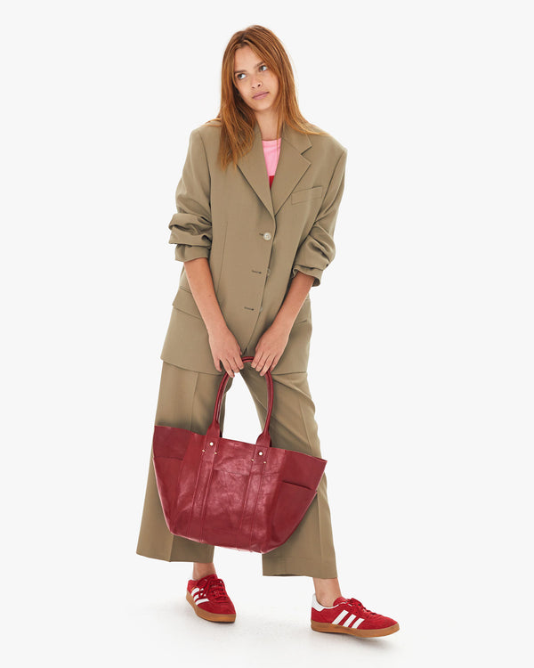 Aurelia wears a khaki suit and holds the Oxblood Rustic Le Slim Box Tote