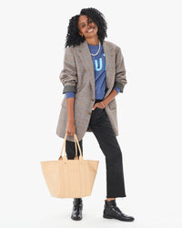 Mecca in a long blazer and black straight leg pants with the Undyed Veg Le Slim Box Tote in her right hand. her left hand is in her pants pocket