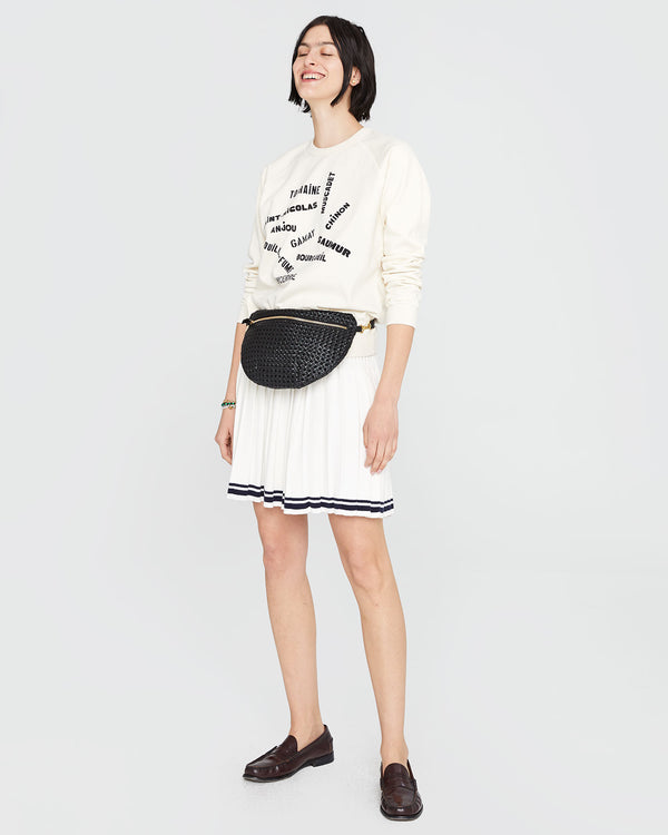 Athena wearing the Sweatshirt in Cream with Valle de Loire with a white tennis skirt and the black rattan grande fanny around her waist