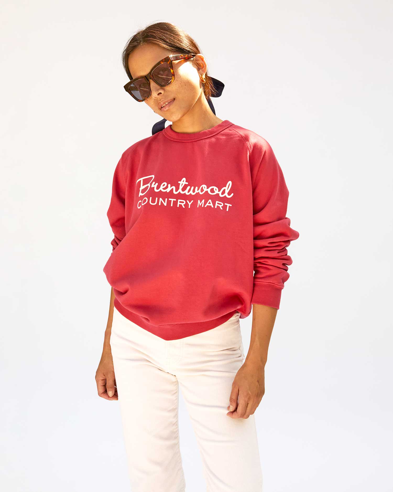 Maly wearing brown sunglasses with the  Brentwood Red w/ Cream BCM Sweatshirt, white jeans with her hands at her side