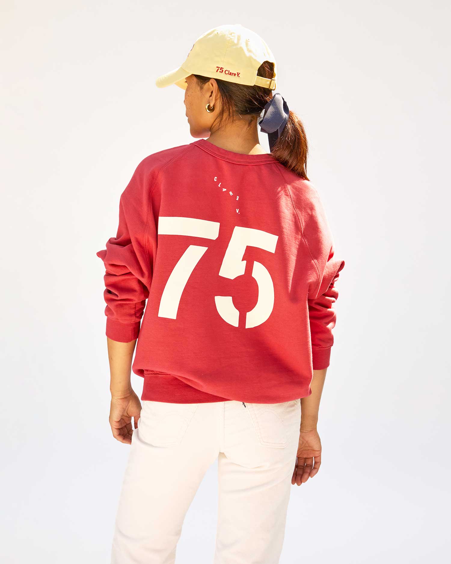 back view of Maly in the  Brentwood Red w/ Cream BCM Sweatshirt with white jeans and the BCM Baseball hat