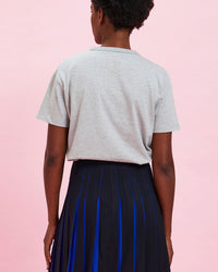 back view of the model wearing the Grey w/ Cobalt Bourgeoisie Sauvage Tee tucked in to the pleated skirt 