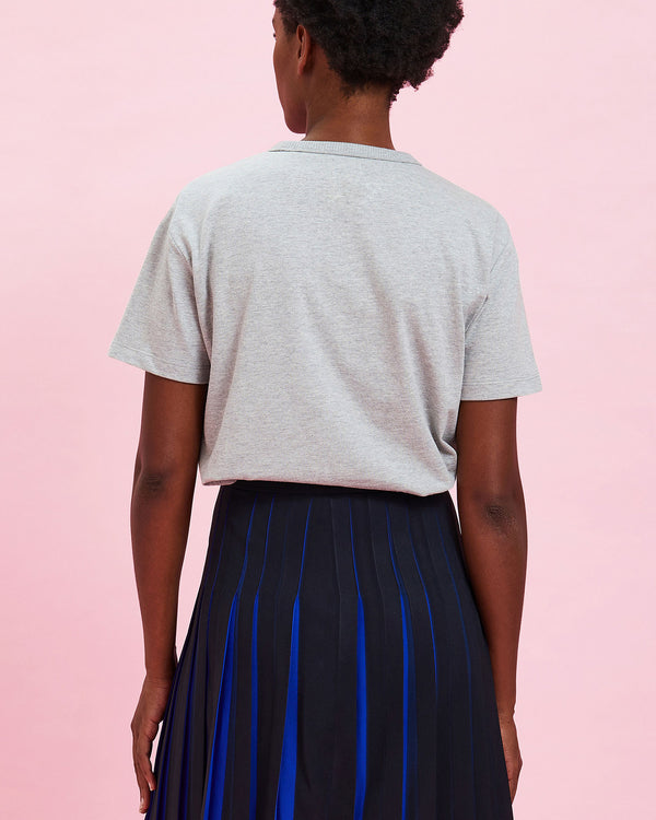 back view of the model wearing the Grey w/ Cobalt Bourgeoisie Sauvage Tee tucked in to the pleated skirt 
