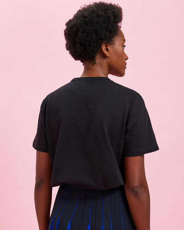 back view of the model wearing the Black w/ Cream Charmant Tee  tucked in to the pleated skirt