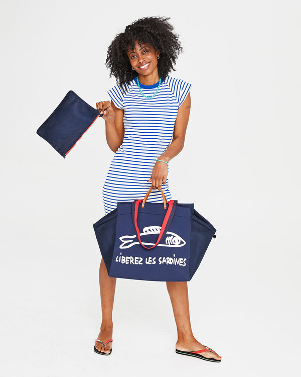 Mecca swinging the Navy Flat Clutch with Tabs  with one hand and carrying the Navy Liberez Les Sardines Trucker Beach Tote via the top handles with the other. 