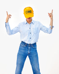 Danica wears the Ciao Trucker Hat in Marigold with a denim shirt and blue jeans