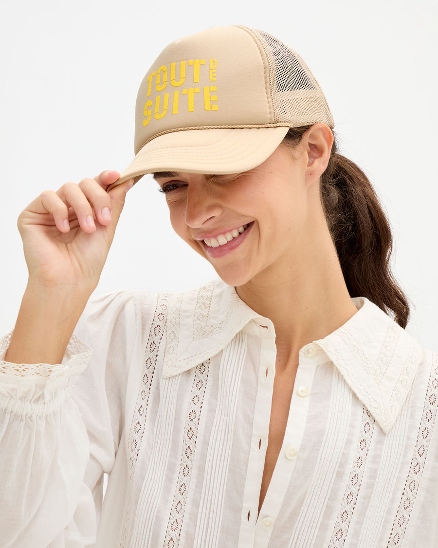 Woman wearing the cream Amélie Blouse and 'Tout de Suite' Trucker Hat. 