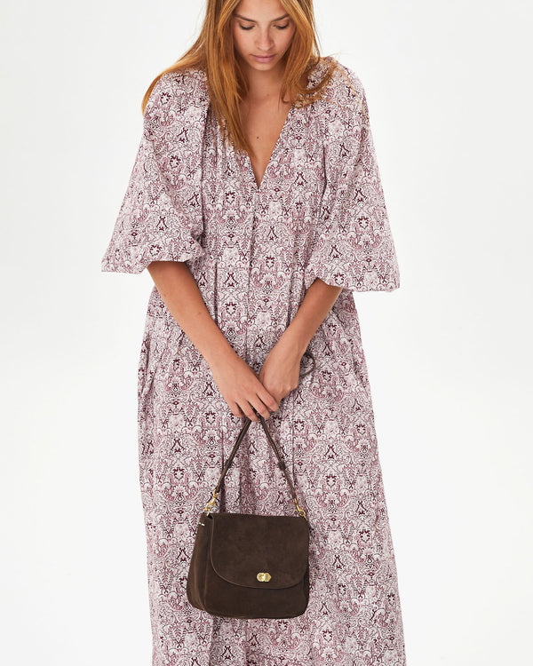 Aurelia wearing a long floral dress holding the Chocolate Suede Turnlock Louis in front of her